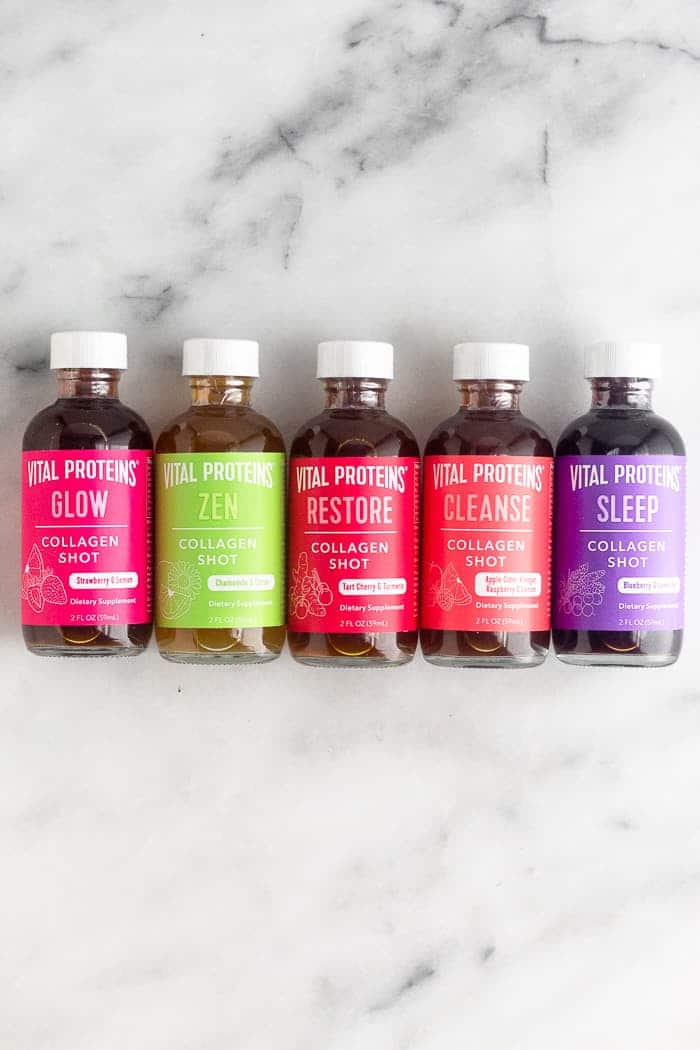 Five different flavors of collagen shots laying down next to each other on a white counter.