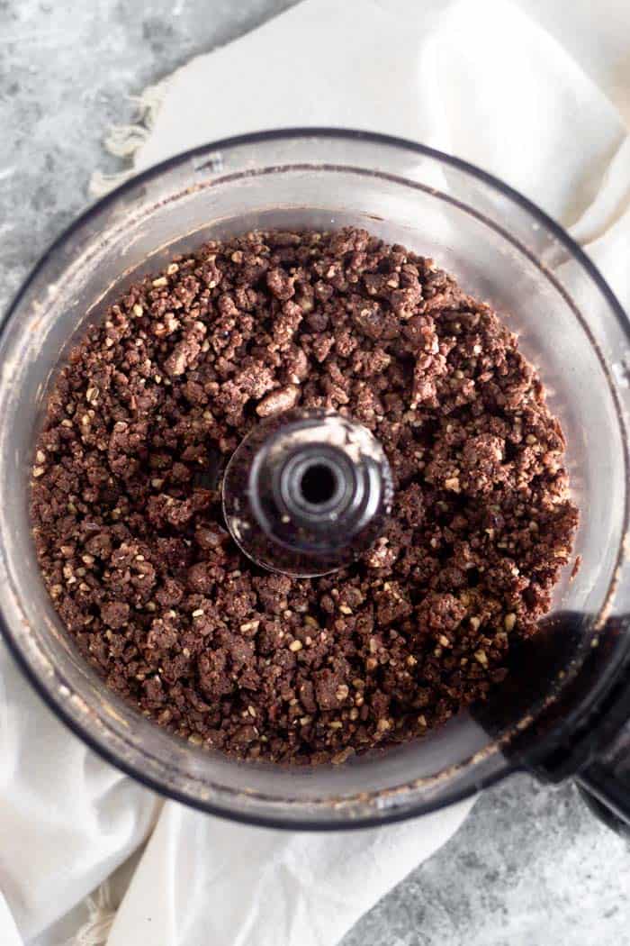 Food processor filled with walnuts and dates that have been broken down into small pieces.