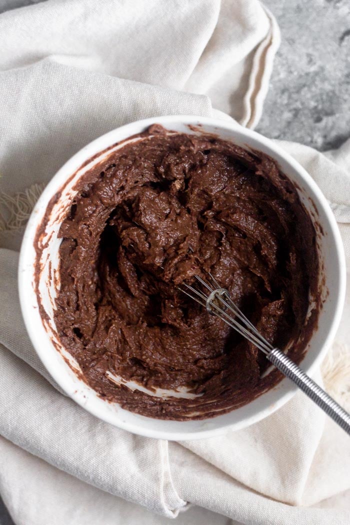 A small bowl of chocolate protein frosting with a small whisk coming out of it.