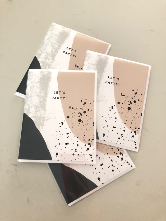 Greeting cards that are white, grey, and beige that say "Let's Party"