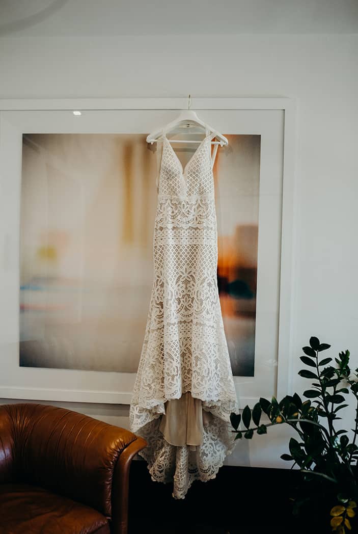Boho lace wedding dress having up on an abstract painting. Next to it is a plant.