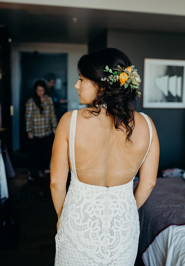 A bride wearing an open back boho wedding dress with her hair pulled back in a messy bun with flowers in it.