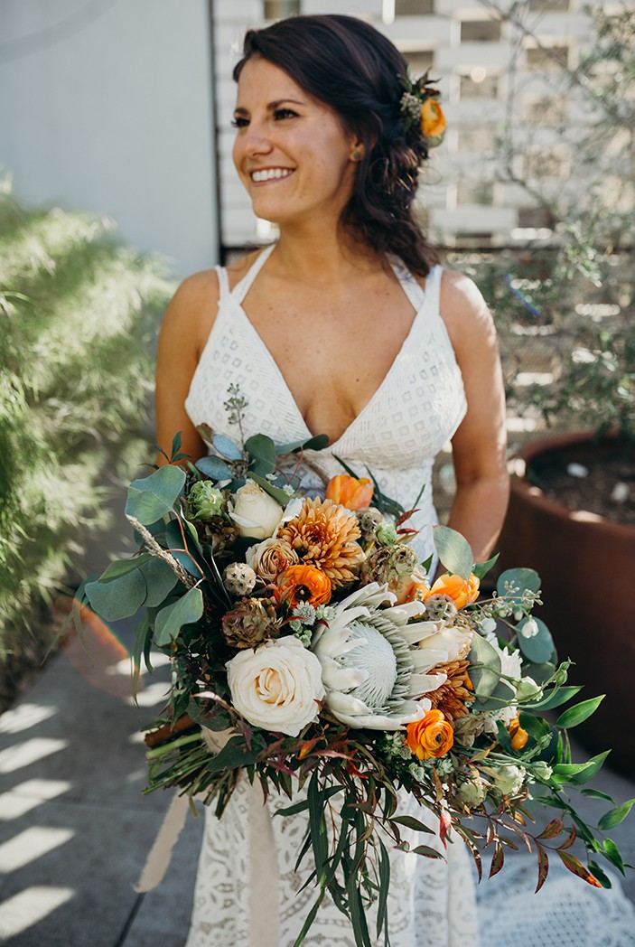 Portrait of a woman in her wedding dressing smiling holding a large bouquet of flowers.