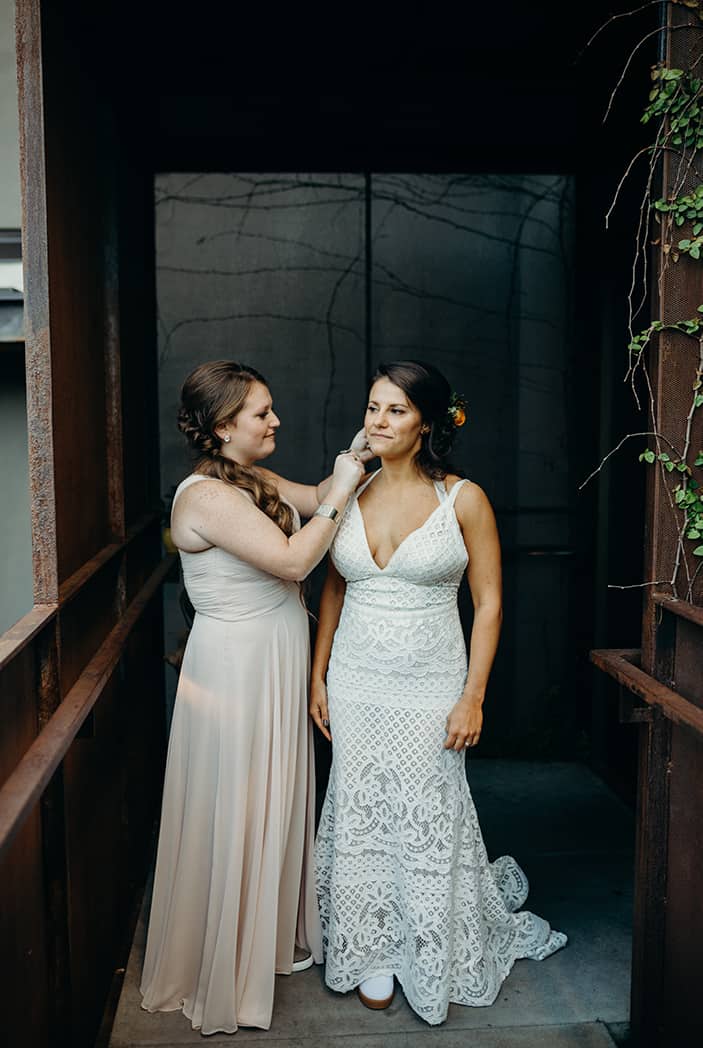 A bride in a boho lace wedding dress. Her sister is next to her and helping her put in her earrings.