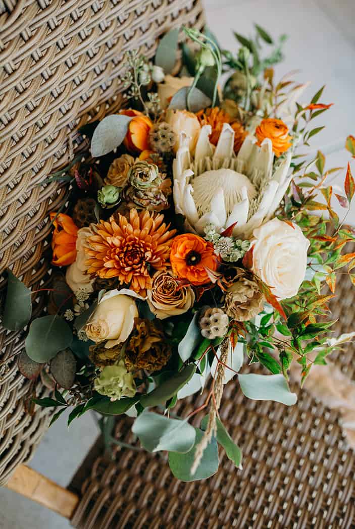 A large bouquet of wedding flowers consisting of whites, oranges, and greens.