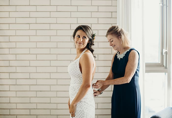 A nothing zipping up her daughter's wedding gown on her wedding day.
