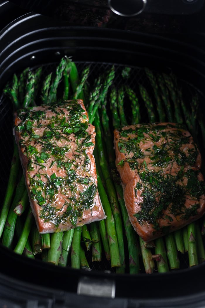 Two dill coated salmon over top asparagus in an air fryer basket