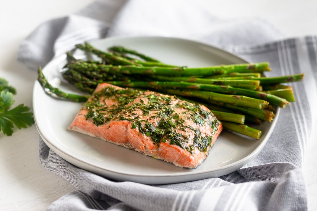 One pan salmon & asparagus made in the air fryer on a white plate sitting on a grey towel.