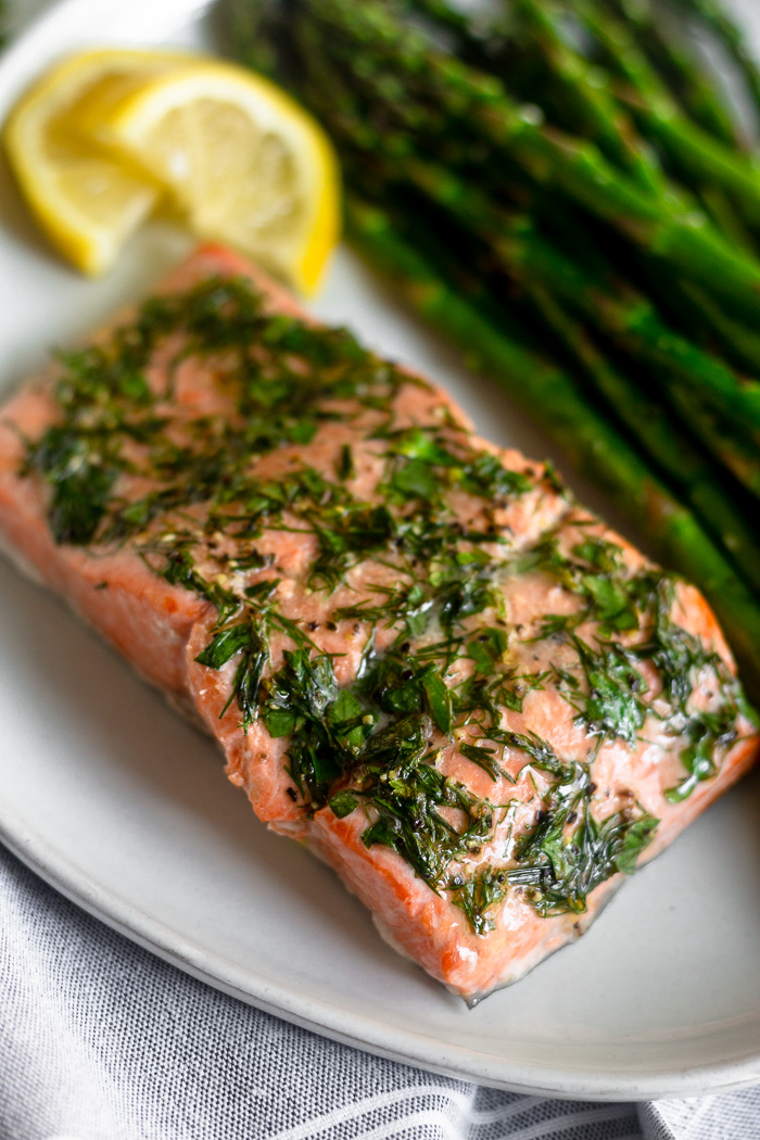A close up of dill coated salmon and asparagus with two lemon wedges on a white plate.