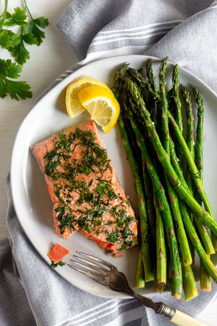 Air fryer salmon and asparagus on a white plate with lemon wedges. There is a fork resting on the plate with a bite out of the salmon.