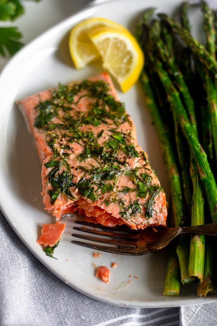 Air fryer salmon ans asparagus on a white plate. There is a bite out of the salmon with a fork resting on the plate.
