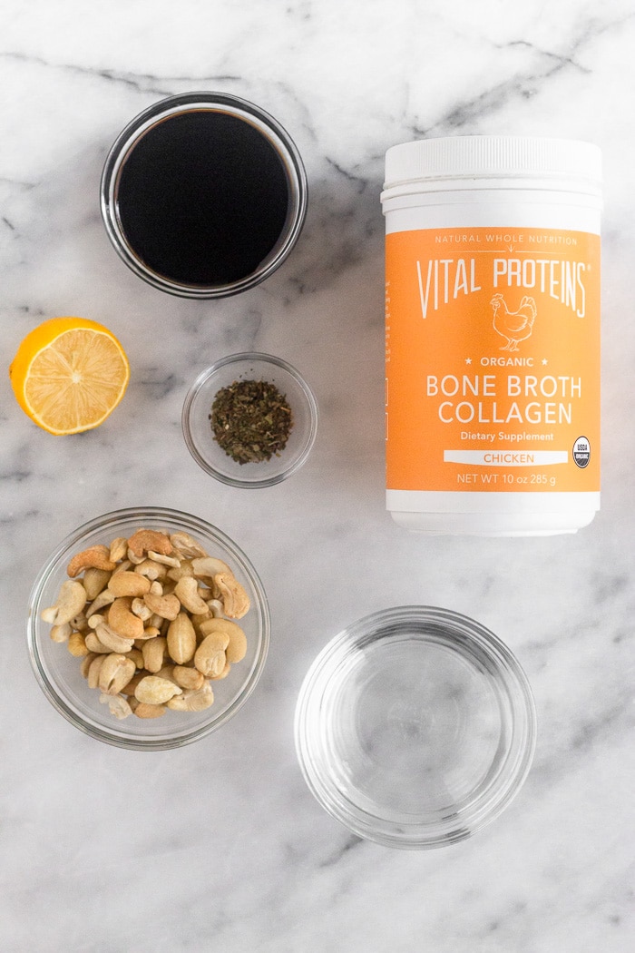 White marble counter filled with Vital Proteins bone broth collagen, water, balsamic vinegar, cashews, lemon, and dried basil.
