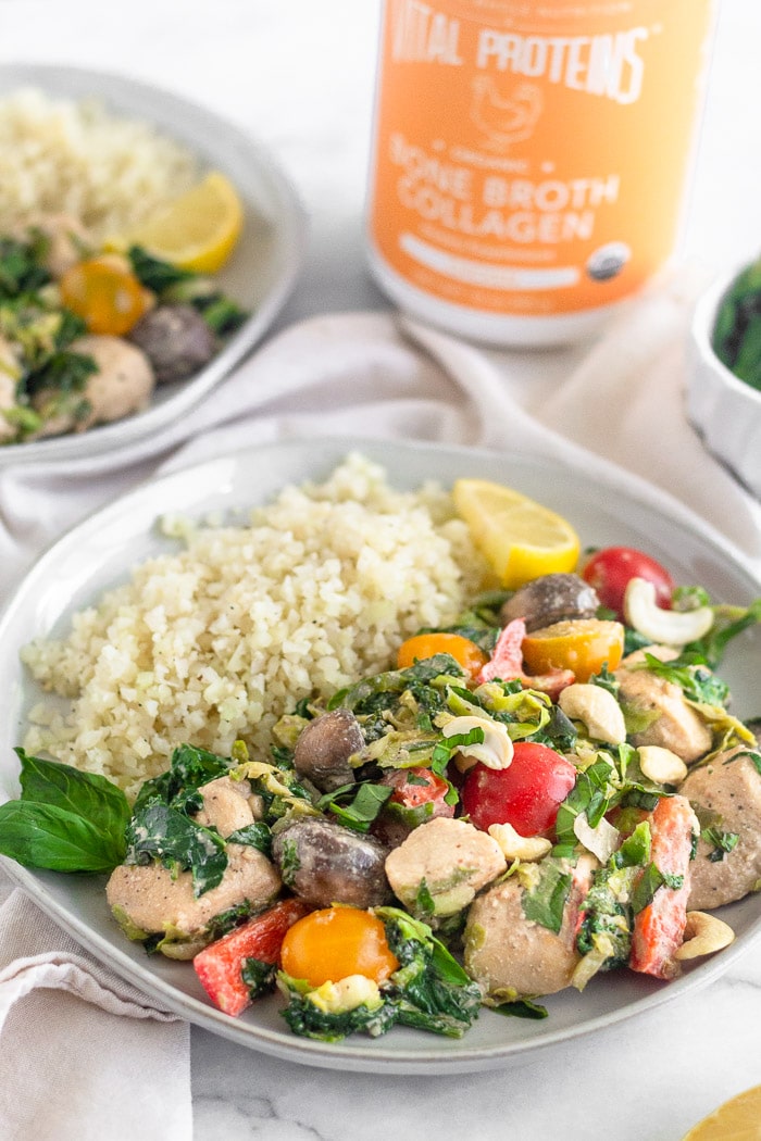 White plate filled with one pan balsamic chicken and veggies, cauliflower rice, basil, and a lemon wedge. Behind it is another plate, container of Vital Proteins bone broth collagen, and a small bowl of basil.