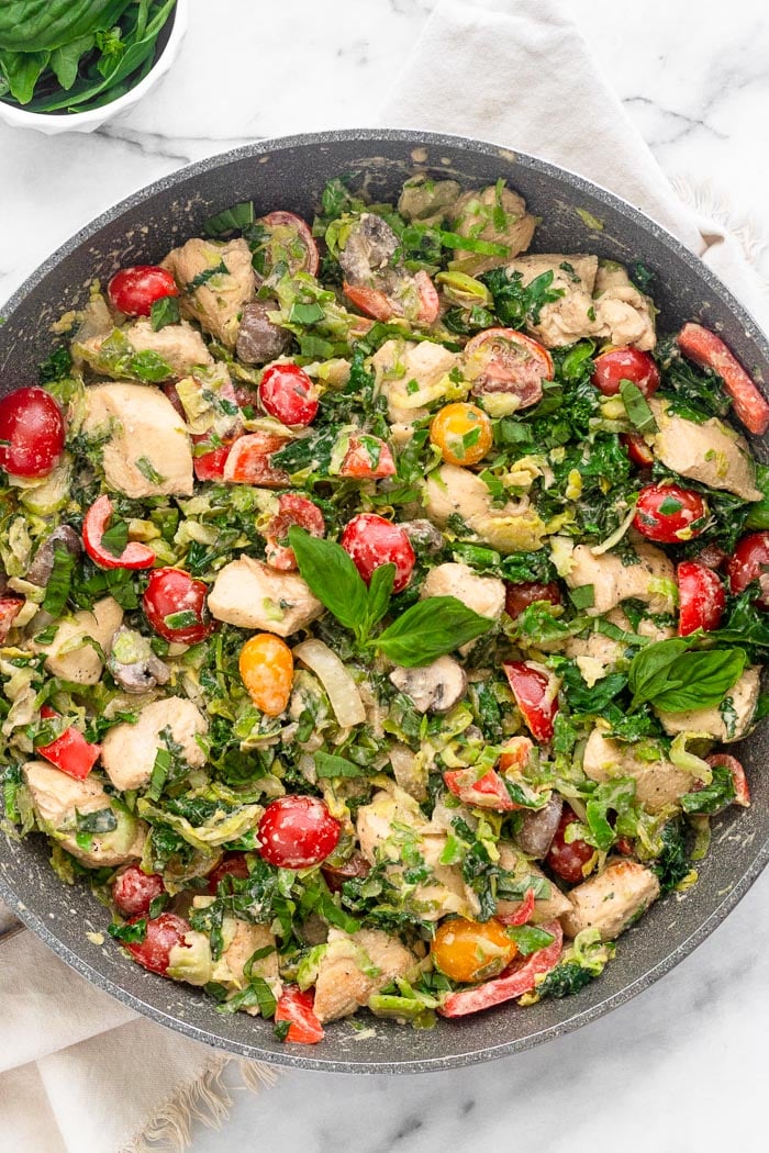 A pan filled with creamy balsamic chicken and veggies made in one pan and done in 30 minutes. It is topped with fresh basil and a small bowl of basil is next to it.