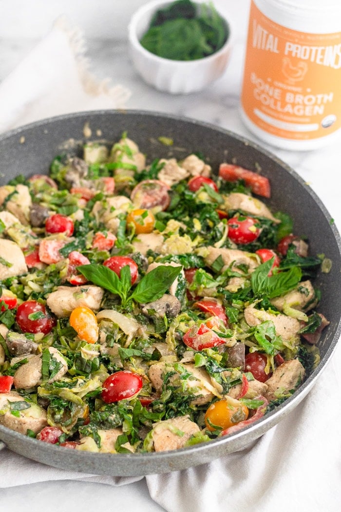 Large skillet filled with creamy balsamic chicken & veggies topped with fresh basil. Behind it is a container of Vital Proteins bone broth collagen and a small bowl of basil.