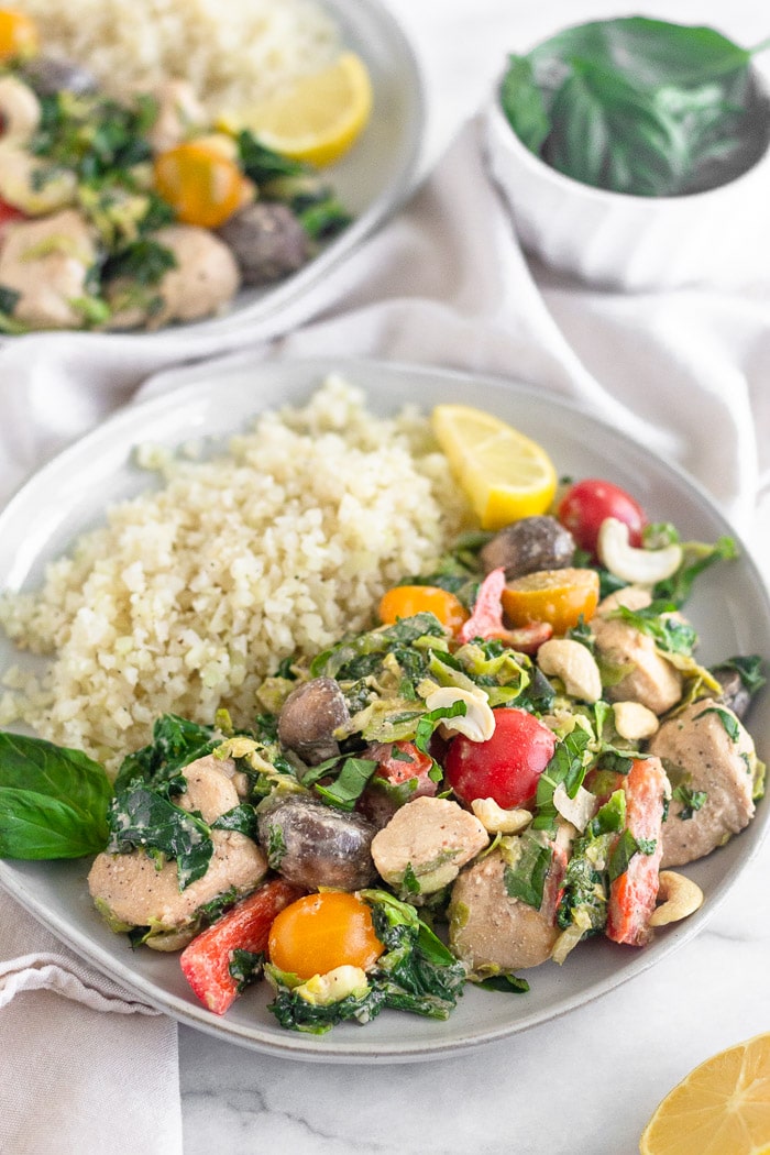 Two white plates filled with creamy balsamic chicken & veggies skillet with cauliflower rice and lemon wedges.