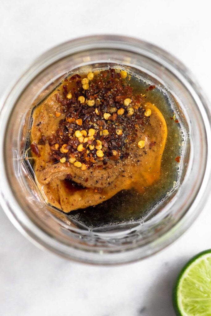 Jar with coconut aminos, lime juice, almond butter, and spices in it. Next to it is half a lime wedge.