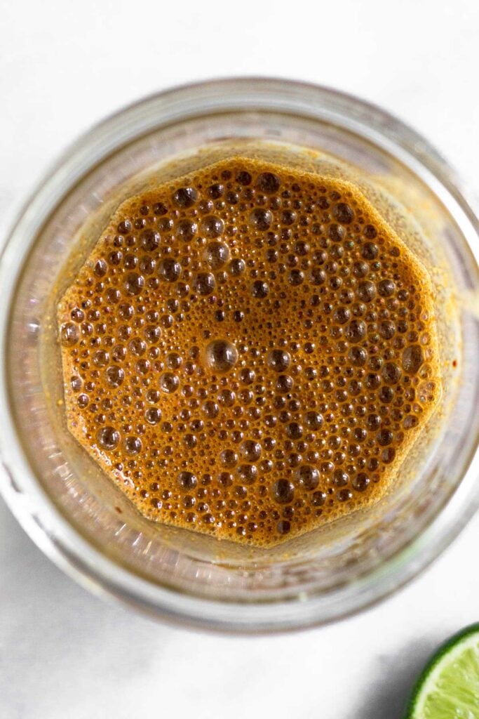 Pad thai sauce in a jar with a lime wedge next to it.