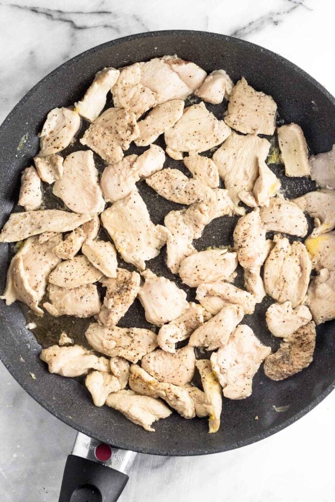 Large skillet filled with bite sized pieces of sautéed chicken.