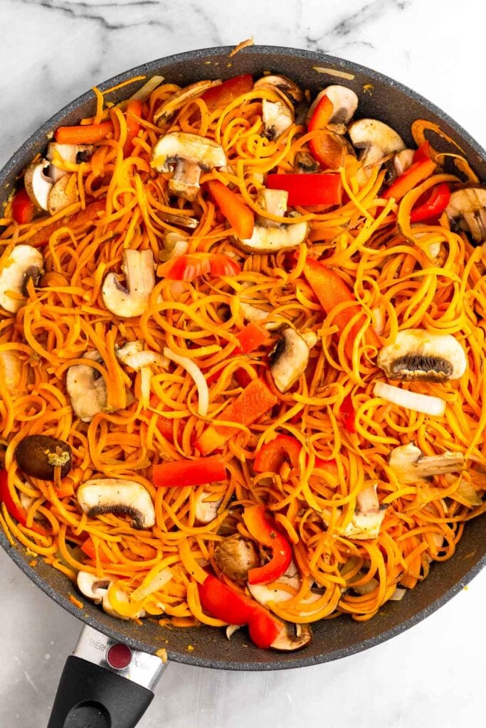 Large skillet filled with sautéed sweet potato noodles, peppers, and mushrooms.
