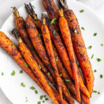 Overhead shot of grilled carrots on a plate topped with fresh herbs.