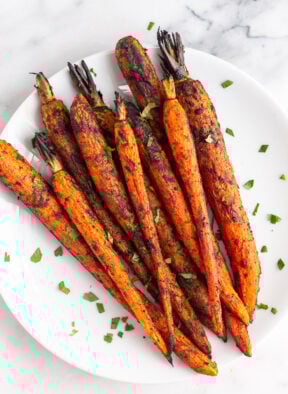 Overhead shot of grilled carrots on a plate topped with fresh herbs.