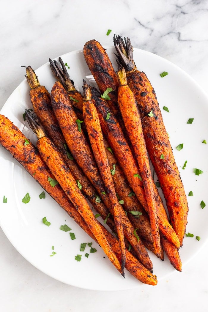 Overhead shot of grilled carrots on a plate topped with fresh herbs.