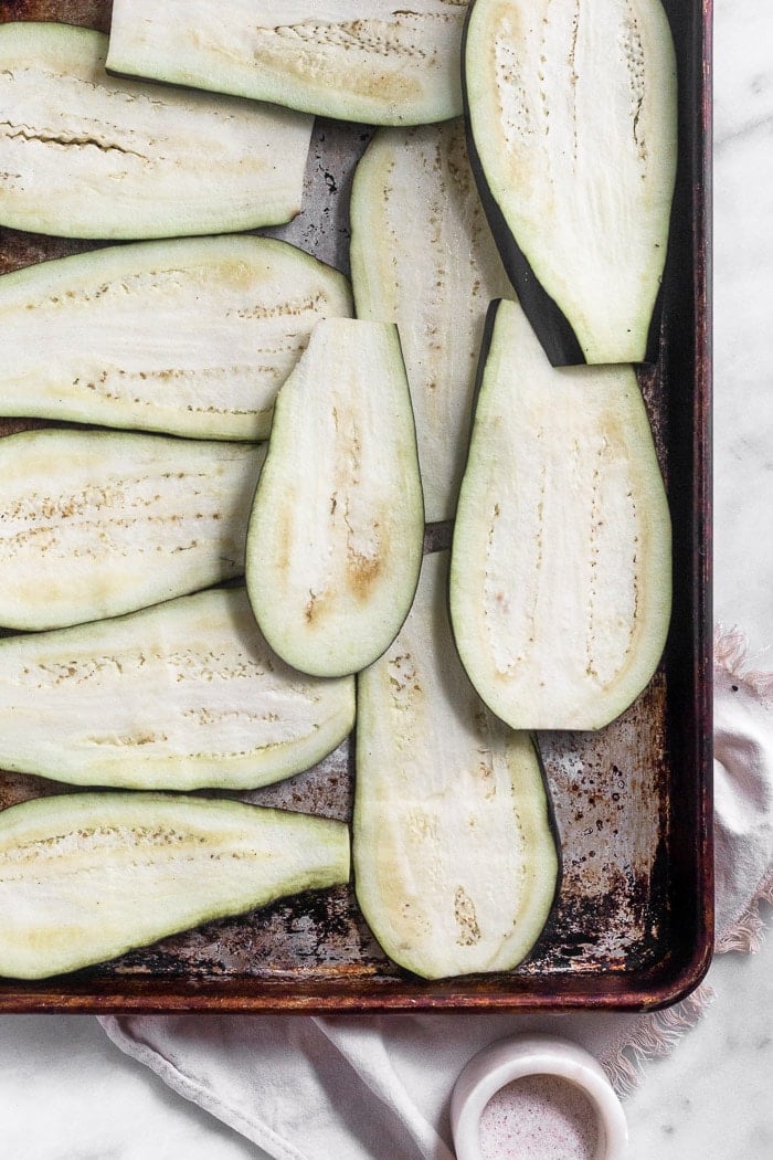 Large baking dish with slices of eggplant on it next to a small white container of salt.