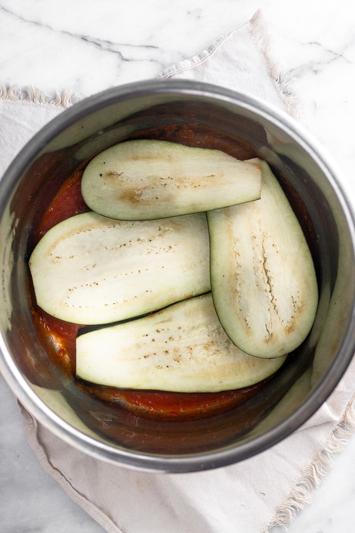 Instant Pot filled with a layer of sauce on the bottom and then topped with a slices of eggplant covering the bottom.