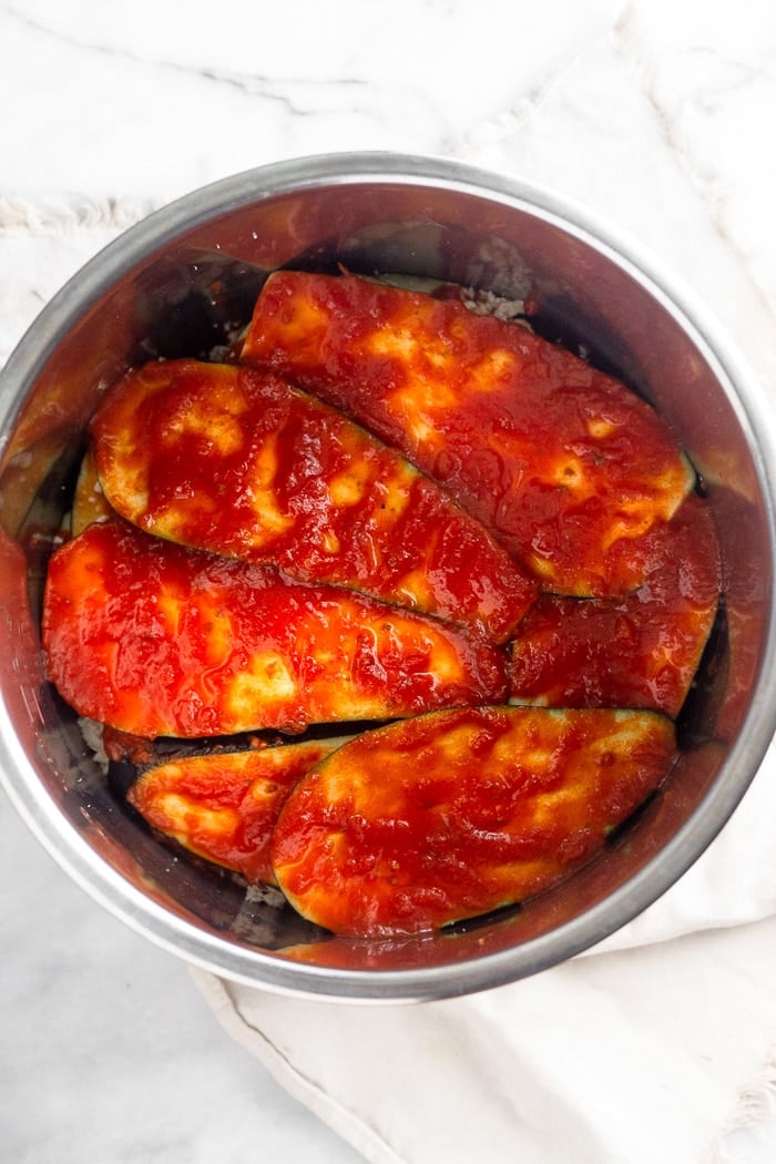 Layers of healthy eggplant parmesan in an Instant Pot covered with a layer of marinara sauce.