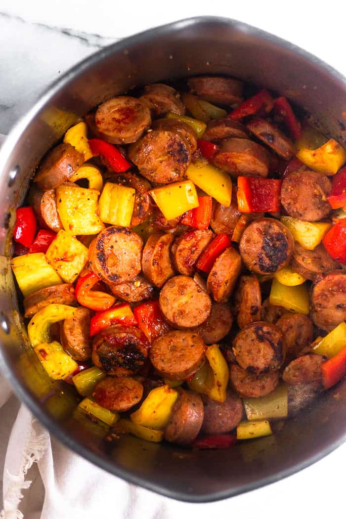 Large stock pot filled with sautéed peppers, onion, and sausage. The pot is sitting on a tan linen.