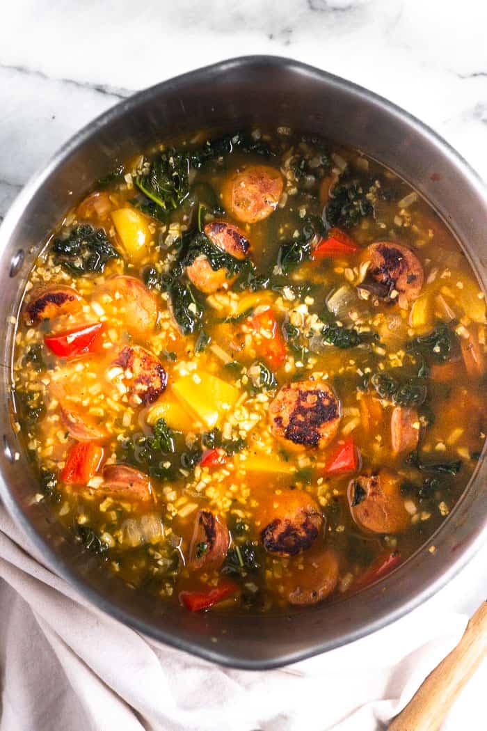 Large stock pot filled with Whole30 sausage, pepper, & rice soup sitting on a tan linen.
