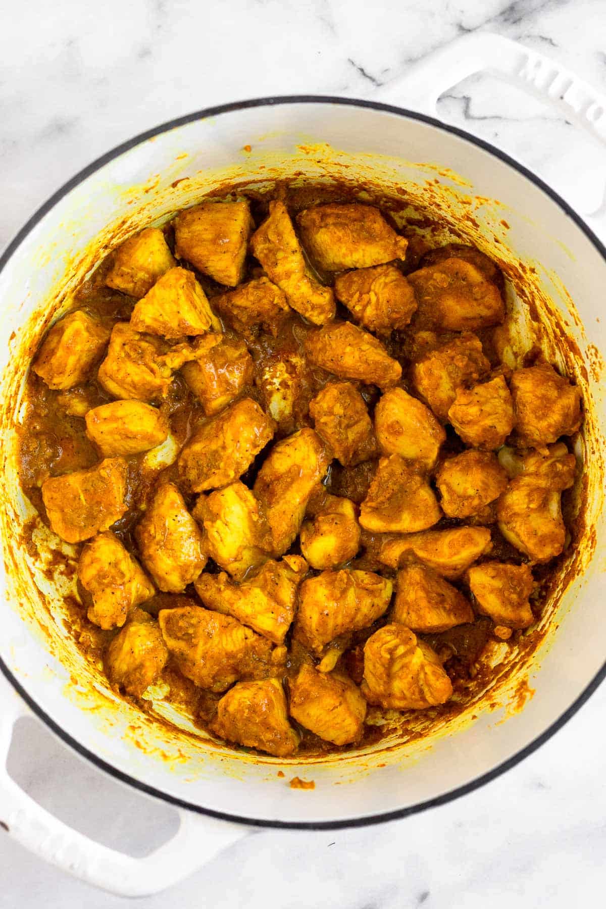 Large pot with sautéed cubed chicken in it covered in spices.