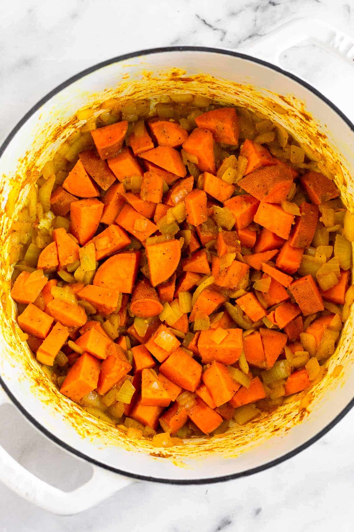 Large pot filled with sautéed onions and sweet potatoes.