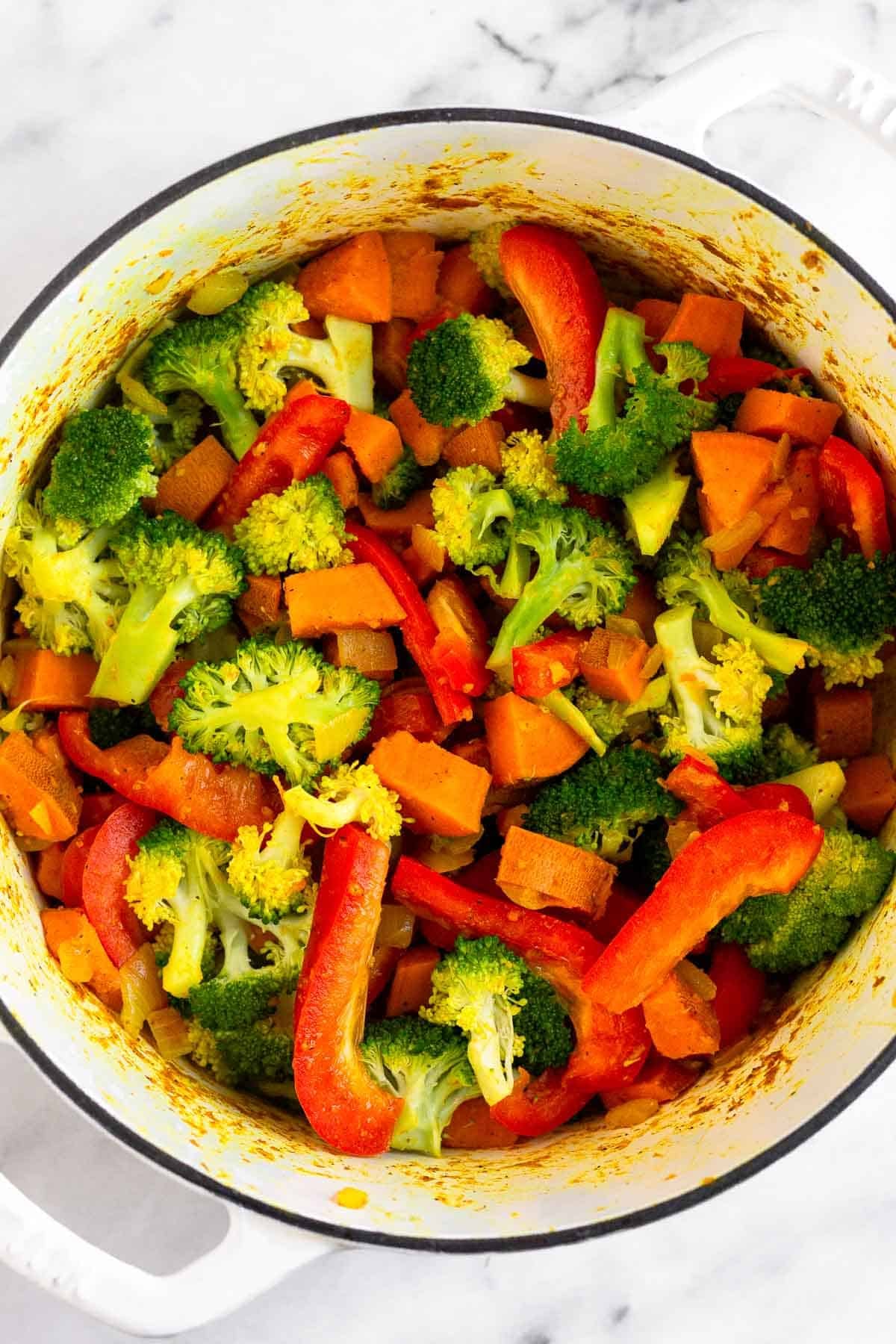 Large pot filled with sautéed sweet potatoes, onion, broccoli, and red bell peppers.