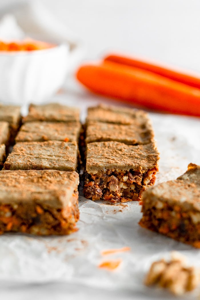 Two rows of no bake carrot cake preotin bars with the first one on the right pulled away from the rest. Behind them are 2 carrots.