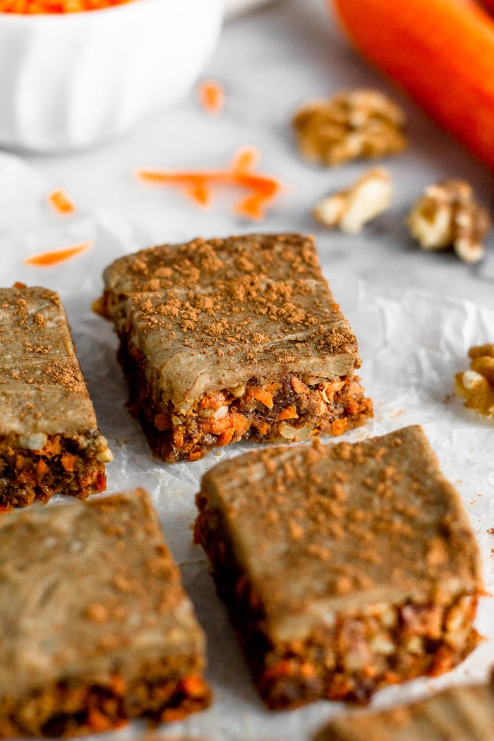 4 no bake carrot cake protein bar next to each other with the focus on the back right one. Behind them are carrots and walnuts.