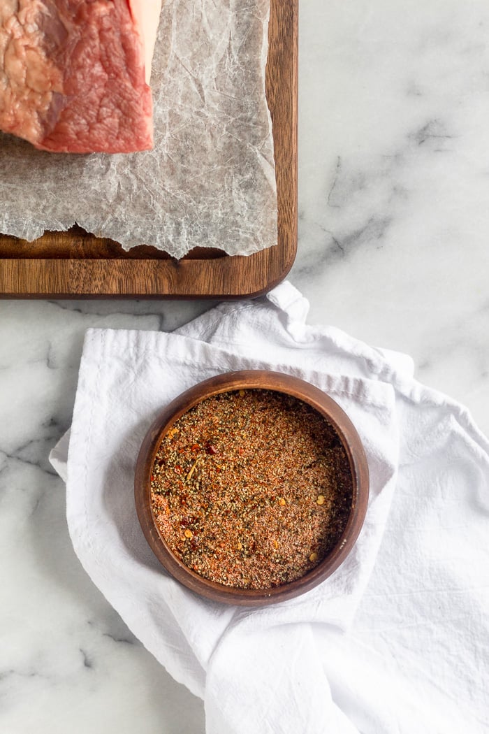 Small bowl of dry rub spices. It is sitting on a white towel with a brisket on a cutting board next to it.