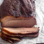 Smoked brisket sitting on a cutting board with a free pieces cut from it