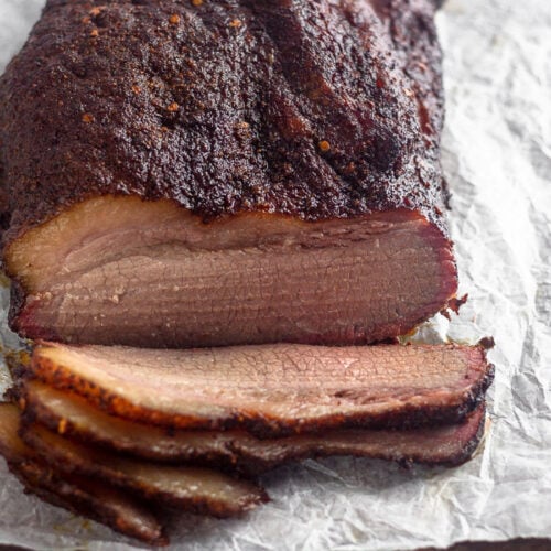 Smoked brisket sitting on a cutting board with a free pieces cut from it