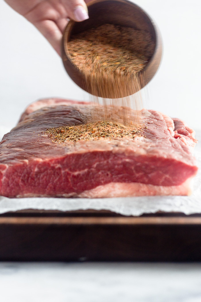 Large piece of raw brisket with a dry rub being poured on it.