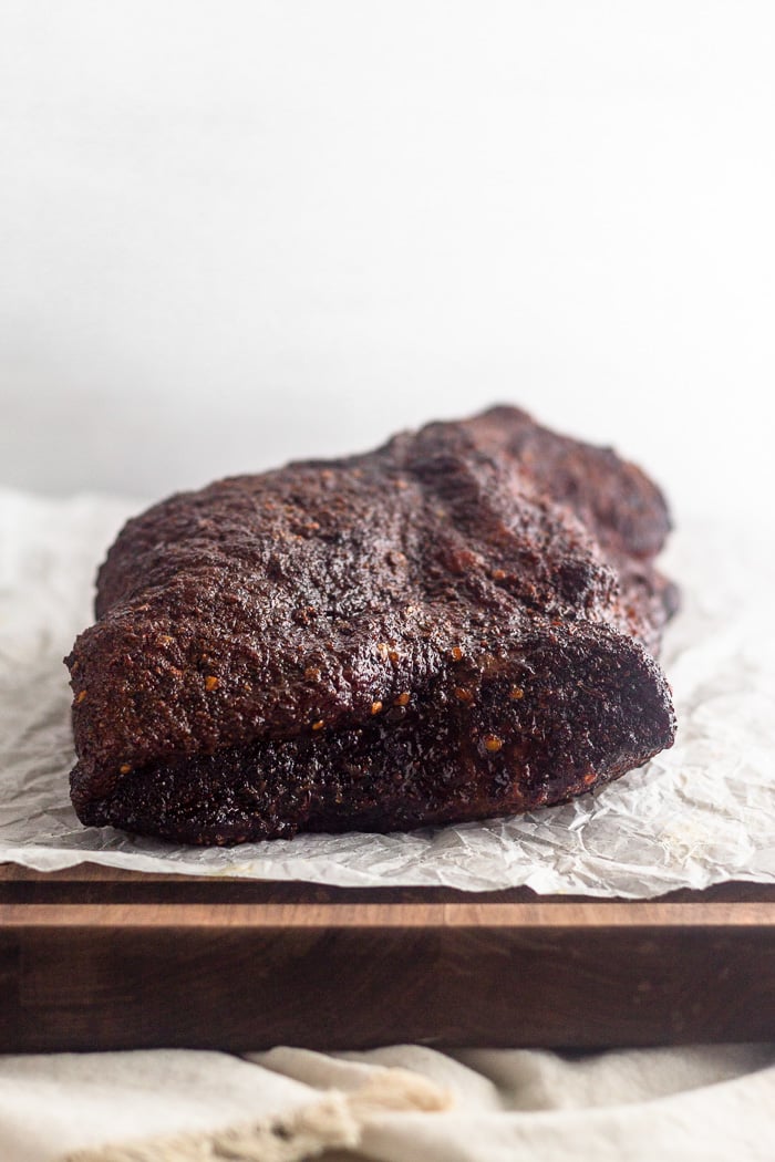 Smoked brisket with dry rubbed sitting on a piece of parchment paper on a cutting board.
