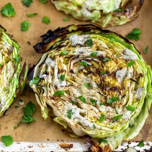 Grilled cabbage steaks on a parchment paper lined baking sheet. They are topped with ranch and fresh herbs.