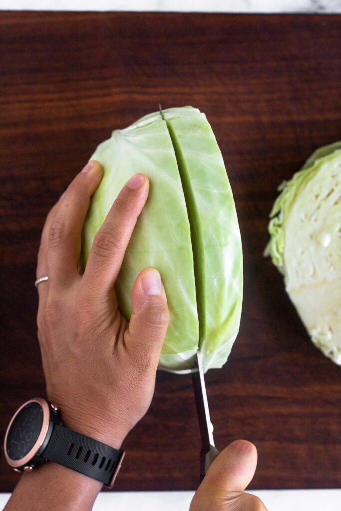 Overhead shot of a head of cabbage that is standing up with someone cutting into it.
