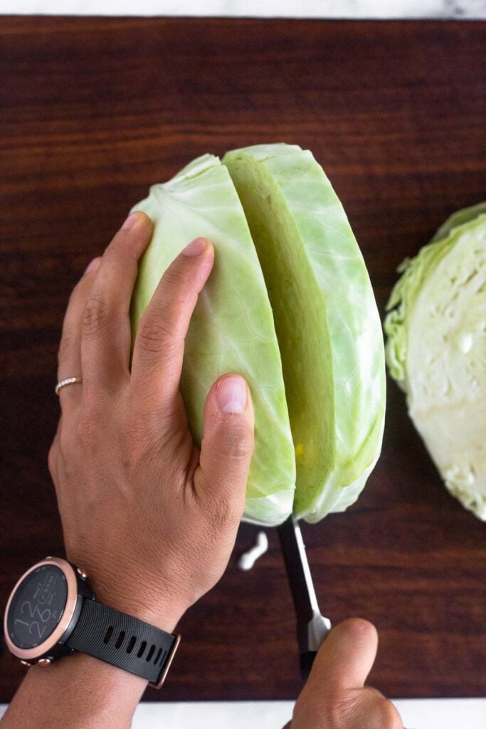 Overhead shot of a head of cabbage that is standing up with someone cutting into it.