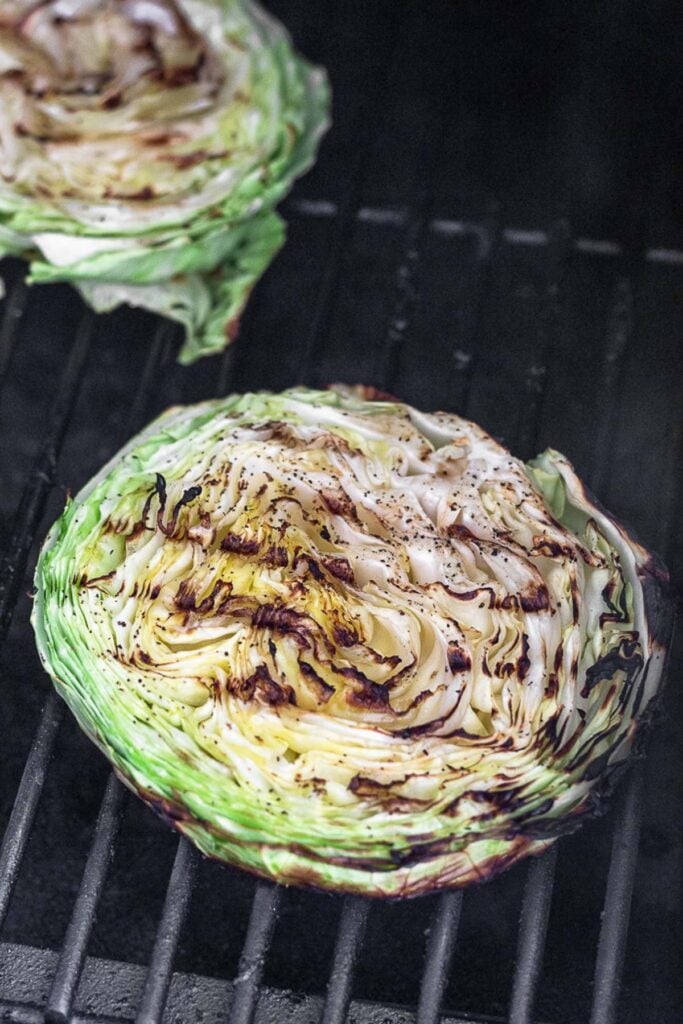 Cabbage steak on a grill with grill marks on it. There is another one off in the background.