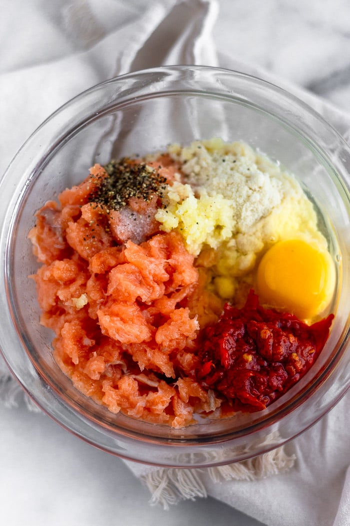Bowl of raw pulsed salmon, almond flour, harissa, egg, minced garlic, and salt and pepper.