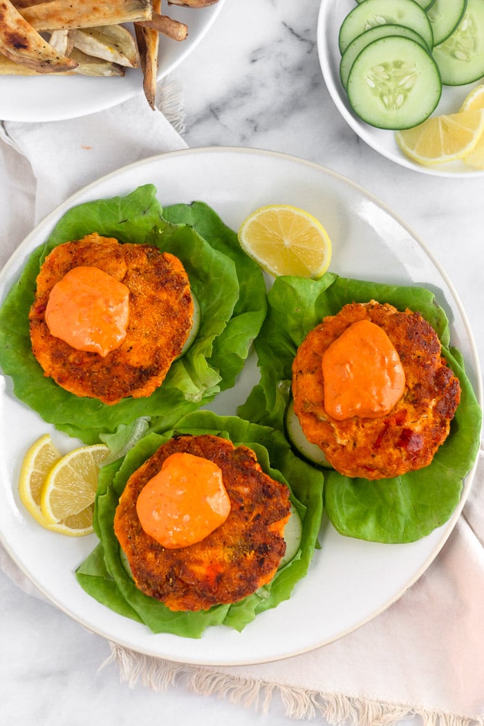 Overhead shot of a plate of harissa salmon burgers with harissa aioli on top. They are sitting on lettuce leaves to make a lettuce wrap.