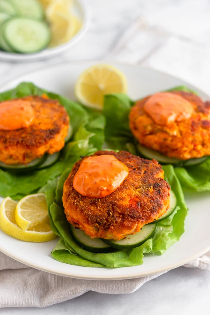 Plate of harissa salmon burger with harissa aioli on lettuce cups with lemon wedges next to them.