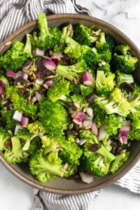 Healthy broccoli salad with raisins and sunflower seeds in a large bowl. The bowl is on a striped kitchen towel.